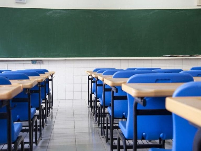 Rows of empty blue chairs and wooden desks face a large green chalkboard in a clean, well-lit classroom with tiled floors and white tiled walls, showcasing the results of expert Commercial Cleaning and Property Maintenance.