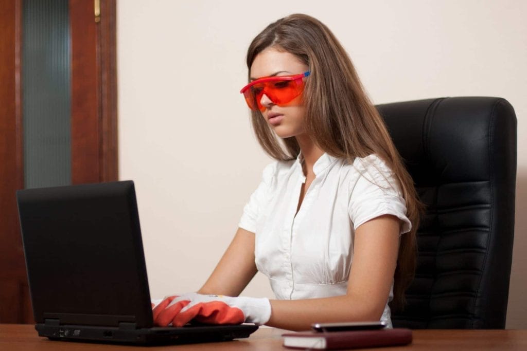 Woman in white shirt sitting in an office chair at a desk and laptop, wearing gloves - Professional office cleaning - Evergreen Maintenance commercial cleaning and janitorial services.