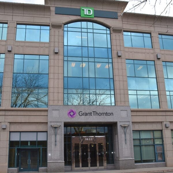 The front of a modern office building with large windows. Signs for TD and Grant Thornton are displayed above the entrance, which has glass double doors and the street number 1633—spotless thanks to regular commercial cleaning.