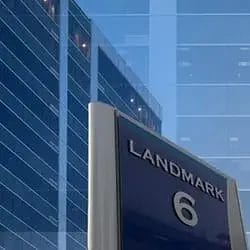 A blue and silver sign reading "LANDMARK 6" stands in front of a modern glass office building reflecting the clear, blue sky, showcasing the property's impeccable appearance thanks to regular commercial cleaning.