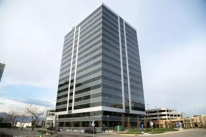 A modern, multi-story office building with reflective glass windows, surrounded by a few leafless trees and a nearby parking structure, stands ready for expert commercial cleaning under a partly cloudy sky.