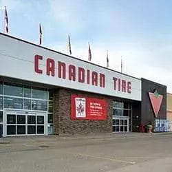 Exterior of a Canadian Tire store featuring large red letters spelling "Canadian Tire" and the store’s red triangle logo above the entrance. Well-kept grounds highlight the importance of property maintenance, with several flags visible on the roof.