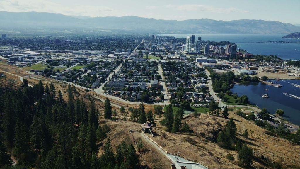 Aerial view of a city by a lake, with a mix of urban and residential areas, surrounded by hills and mountains—an ideal landscape for comprehensive commercial cleaning and property maintenance under a partly cloudy sky.