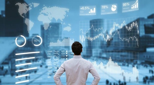 A person in a white shirt looks at transparent digital screens displaying graphs, charts, and world maps, representing data analytics and financial statistics, with a cityscape in the background.