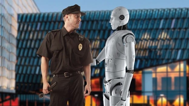 A police officer in uniform stands facing a humanoid robot outside a modern glass building, appearing to interact or converse with it.