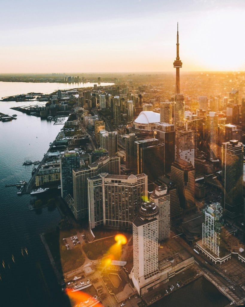 Aerial view of downtown Toronto at sunset, featuring the CN Tower, high-rise buildings maintained by Evergreen Building Maintenance, Lake Ontario, and the shoreline with sunlight casting a warm glow over the city.